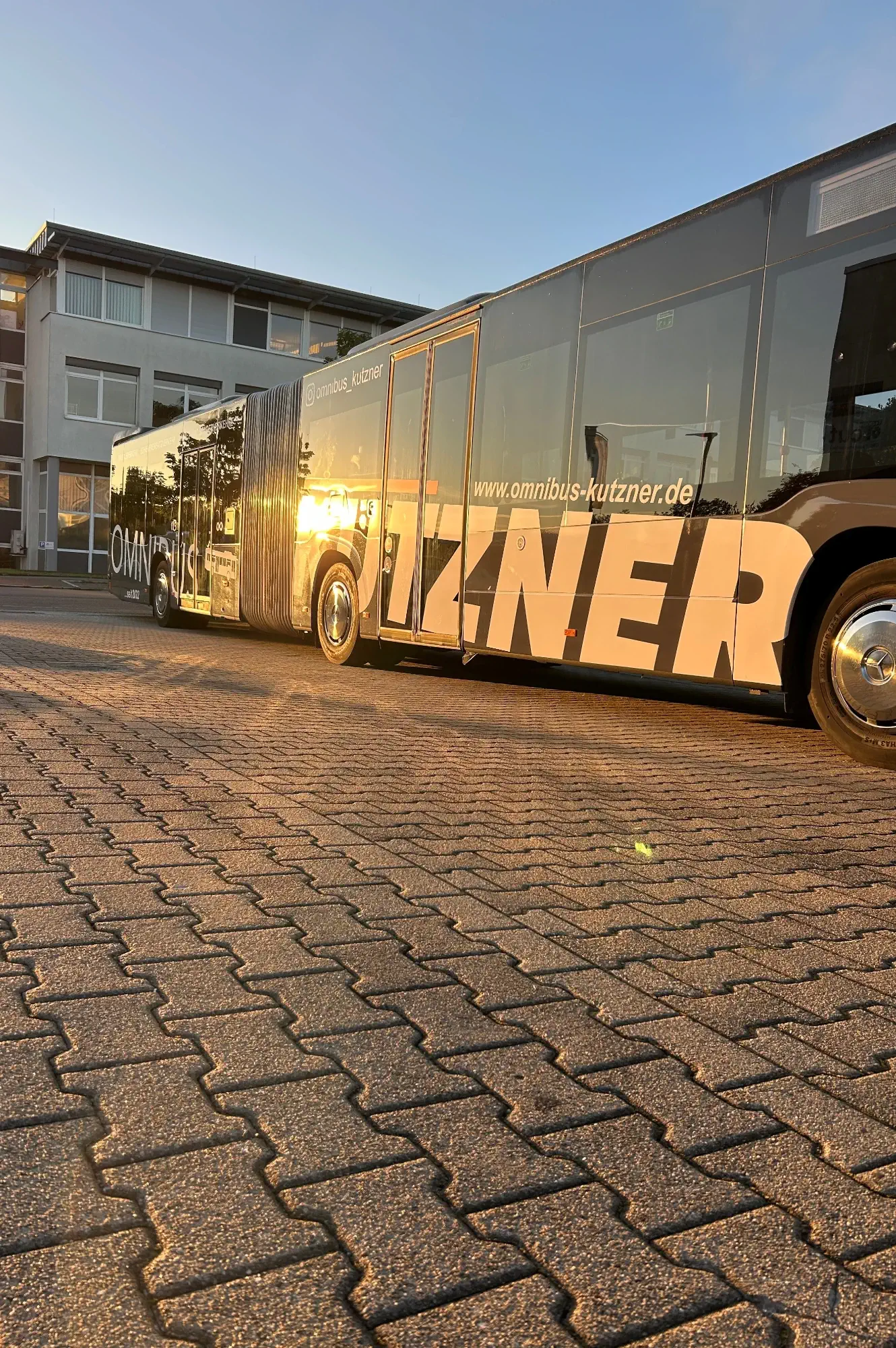 Ein von der Abendsonne beschienener Kutzner Bus im Linienverkehr, schräg von hinten fotografiert.