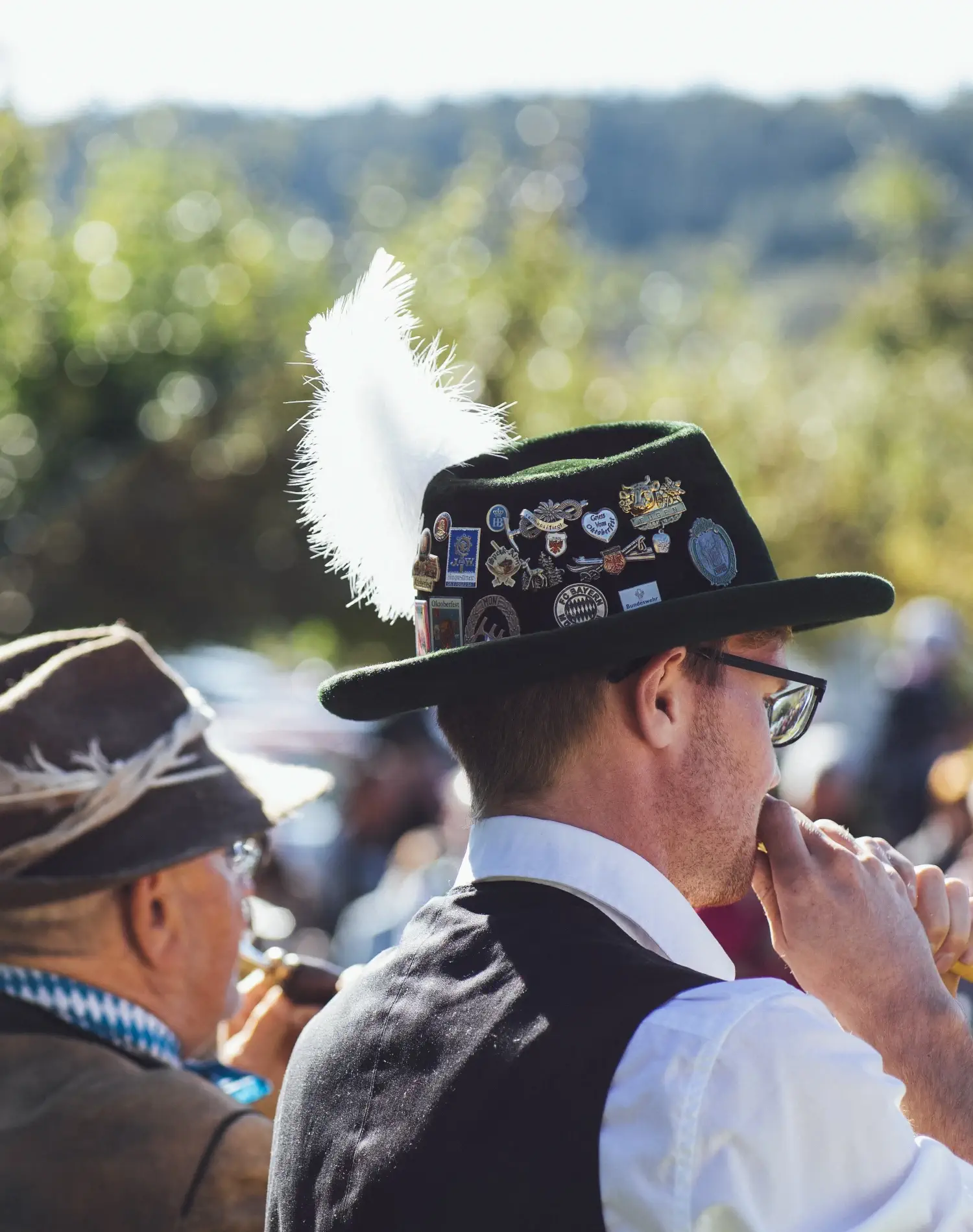 Zwei männliche bayerische Musiker in Tracht mit Blasinstrumenten und von hinten fotografiert.