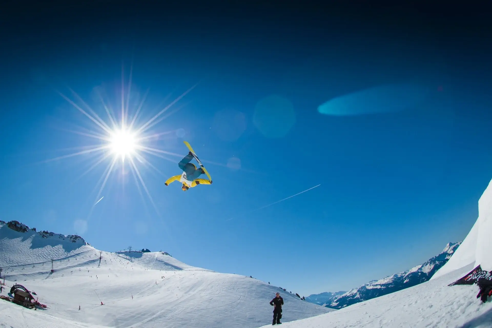 Ein Snowboarder beim Rückwärtssalto vor strahlend blauem Himmel.