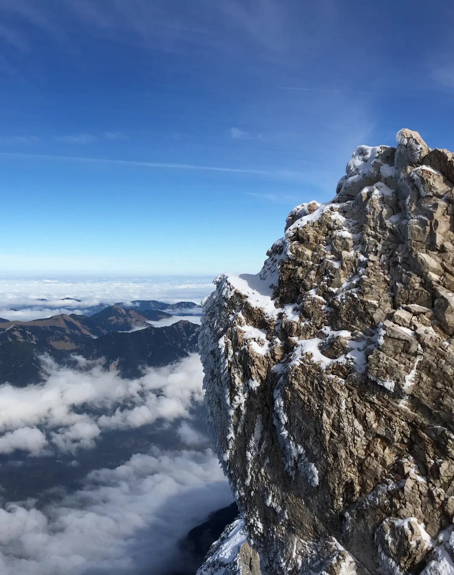 Ein massiver steinerner Berggipfel bei blauem Himmel und über den Wolken